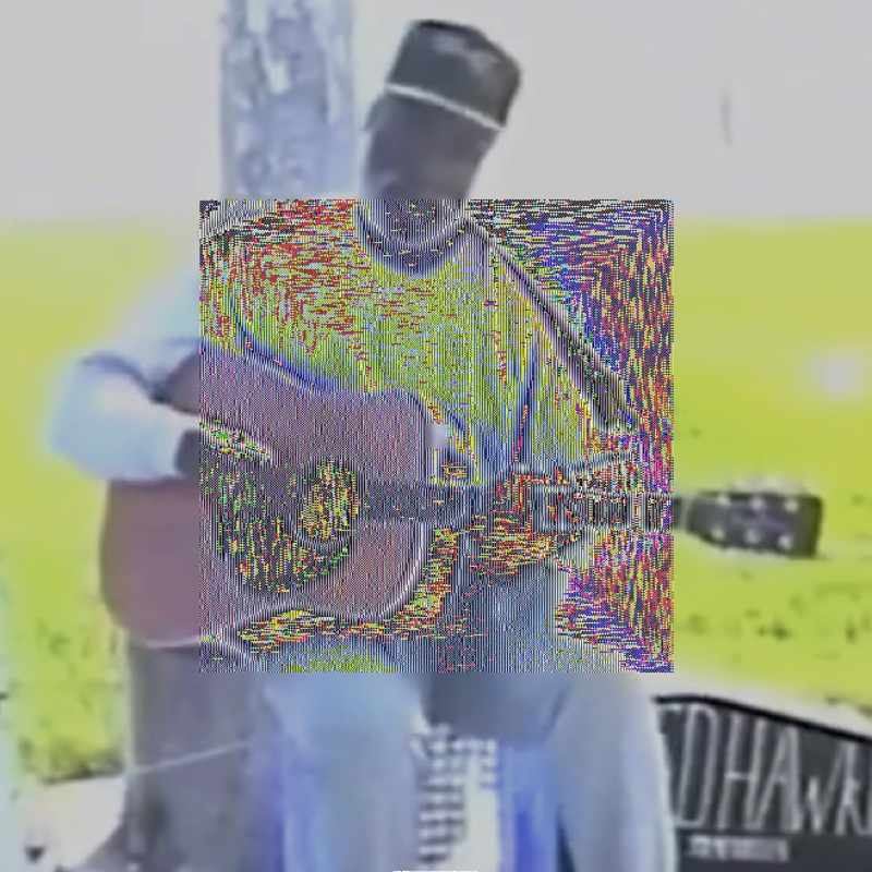 A medium VHS-recorded shot of Ted Hawkins sitting on a makeshift stool on the Venice Beach boardwalk, longsleeve shirt, ballcap, acoustic guitar in hand. The cropped letters 'Ed Hawk' can be seen in tall handwriting on a open guitar case on the right side of the image on the ground. The image is sunlit high contrast with a lot of white and green. In the center is a square covering half the image with intense red, blue, yellow, and green noise.
